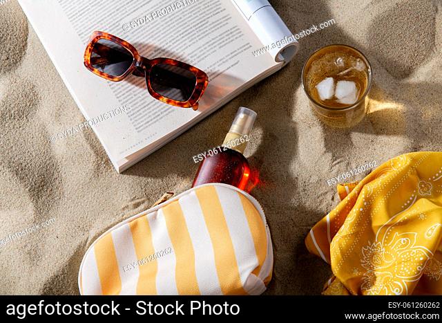 magazine, sunglasses and sunscreen on beach sand