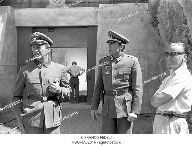 British actor David Niven and American actor Gregory Peck in uniform talking beside British director J. Lee Thompson on the set of the film The Guns of Navarone