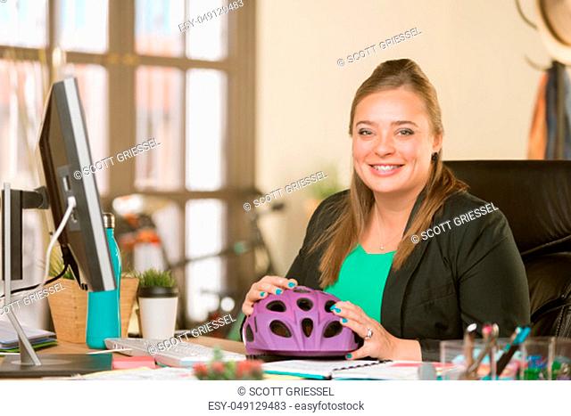 Young creative professional woman at her desk with a bicycle helmet