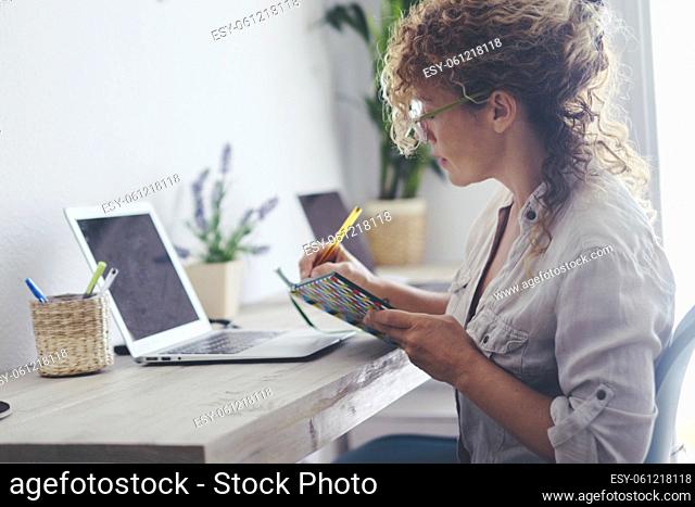 Modern housewife manage family economy at home - single lady use laptop computer and book with pen to takes notes and work - adult female viewed from side...