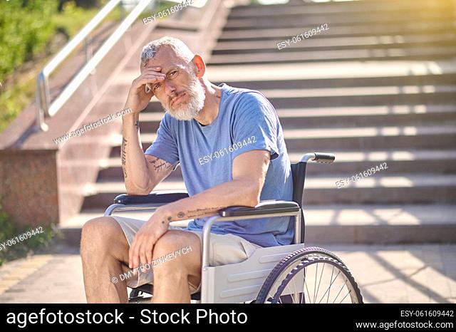 In thoughts. A disabled man in a wheel chair outdoors looking thoughtful