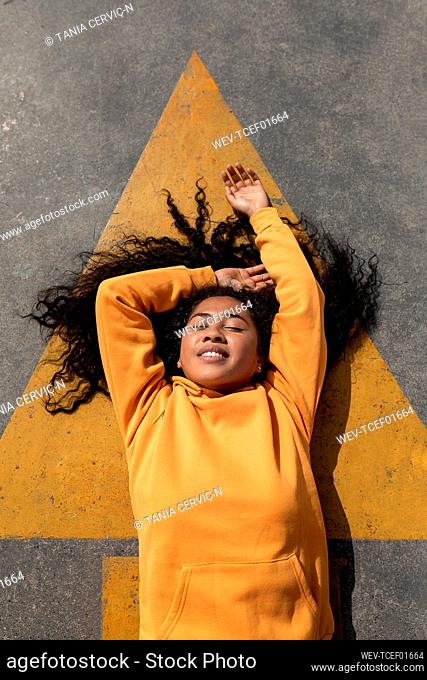 Smiling young woman lying down on footpath