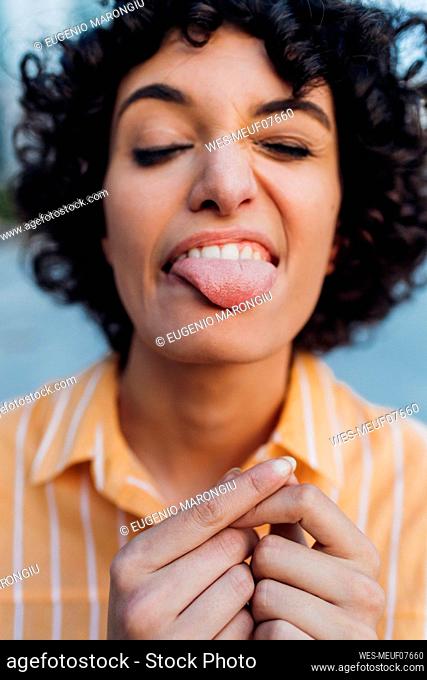 Playful young woman with eyes closed sticking out tongue