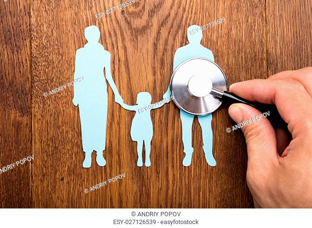 Person Holding Stethoscope On Family Papercut At Wooden Desk