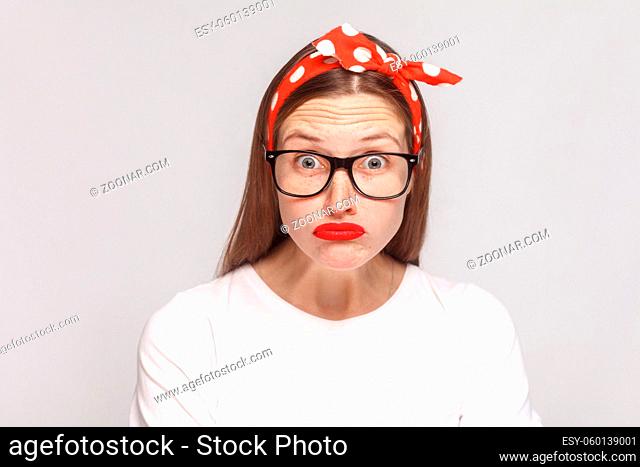 big eyes shocked face of beautiful emotional young woman in white t-shirt with freckles, black glasses, red lips and head band looking at camera