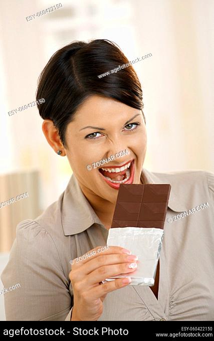 Closeup portrait of excited young woman biting chocolate
