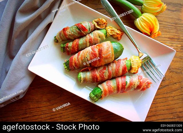 Grilled zucchini fries wrapped in a bacon on white plate