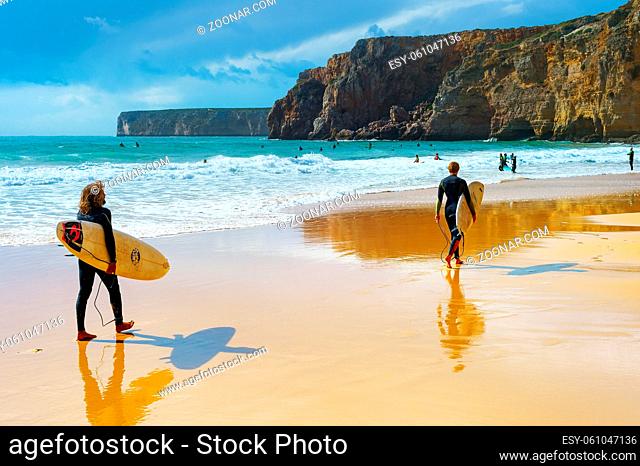 SAGRES, PORTUGAL - OCTOBER 30, 2018: Young men walking by sandy beach with surfboard. ALgarve is a famous surfing destination in Portugal