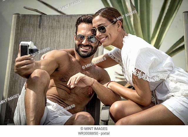 A couple sitting on sun loungers posing for a selfie