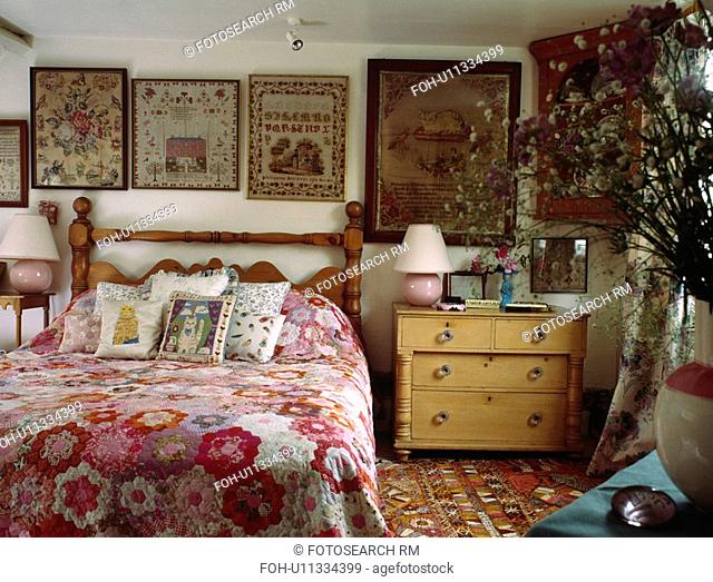 Framed antique samplers behind bed with patchwork quilt in country bedroom with pine chest of drawers