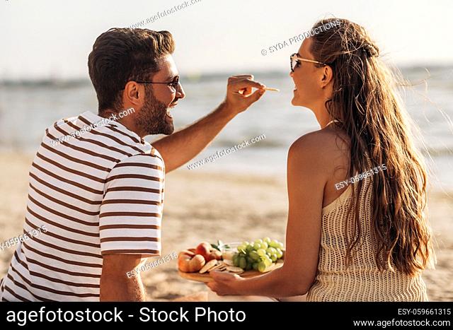happy couple with food having picnic on beach