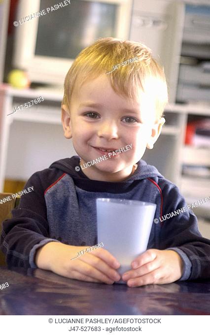 3 year old boy smiling into camera at nursery, holding a cup of milk