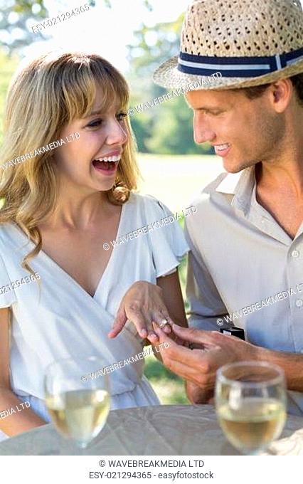 Man placing engagement ring on smiling fiancees finger