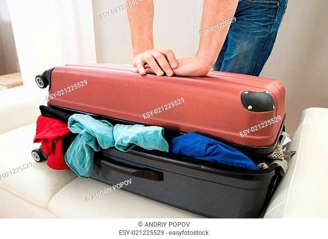 Close-up Of Person Hand Trying To Close Suitcase On Sofa