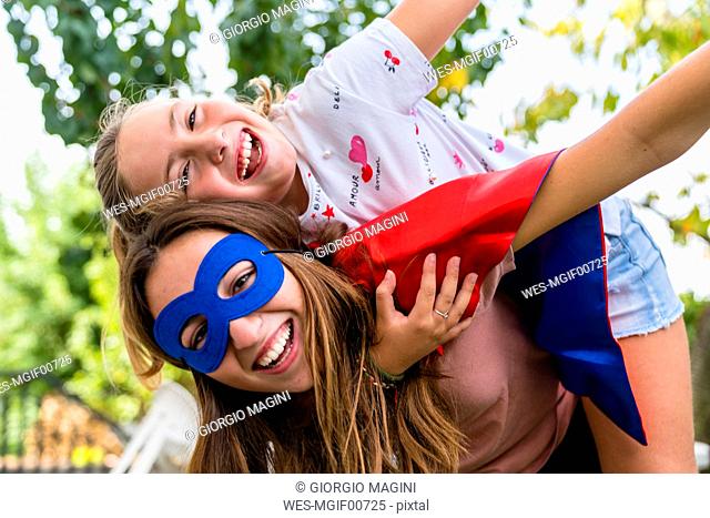 Two happy sisters with eye mask playing in garden