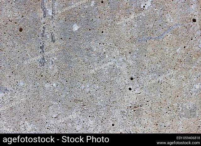 A flat grey concrete surface. The surface is textured and covered in holes from lots of tiny air bubbles