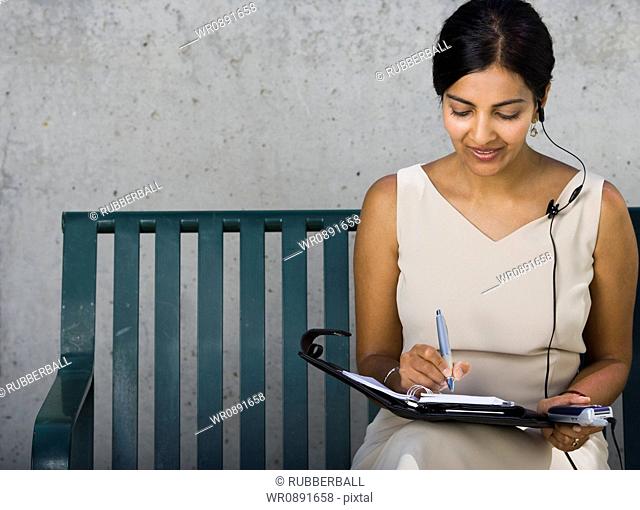 Businesswoman sitting on a bench and writing in a diary