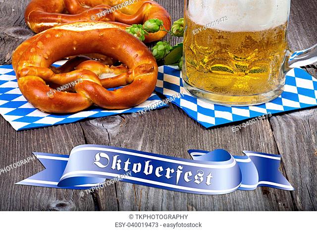 A beer mug and pretzels on napkins with blue and white rhombuses on a rustic wooden table at the bottom a blue banner with the words Oktoberfest