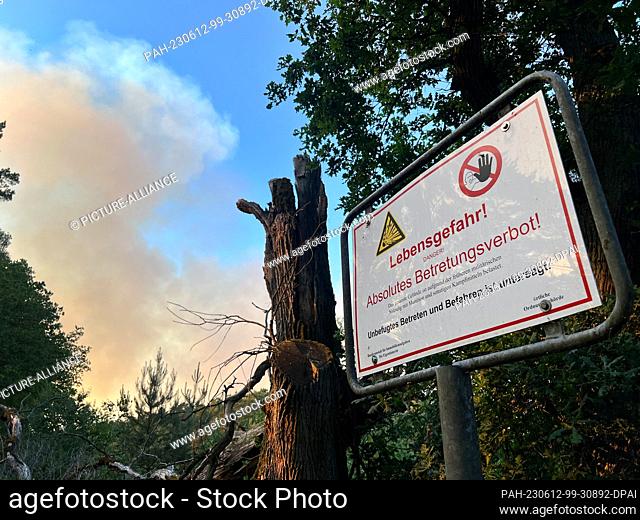 12 June 2023, Mecklenburg-Western Pomerania, Lübtheen: Smoke rises above a wooded area, on the right a warning sign with the inscription ""Danger to life