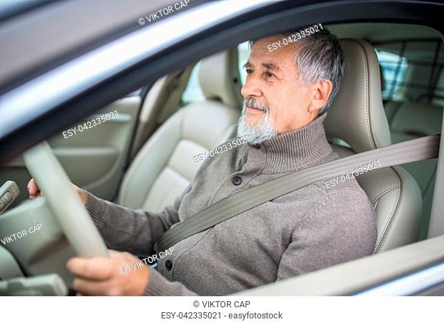 Senior man driving his modern car, going in reverse, watching out not to hit anything or anyone (color toned image; shallow DOF)