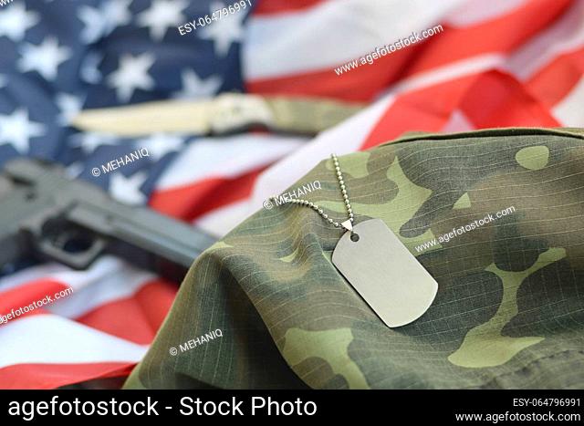 Army Dog tag token with 9mm bullets and pistol lie on folded United States flag and camouflage uniform. A set of US military veteran items or old duty trophy...