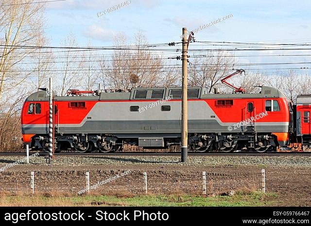 Red locomotive on electricity coming by rail