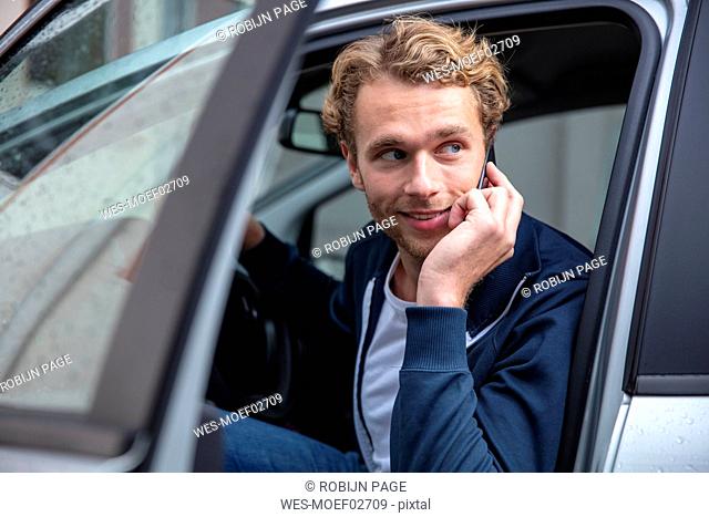 Young man phoning and sitting in car, looking sideways