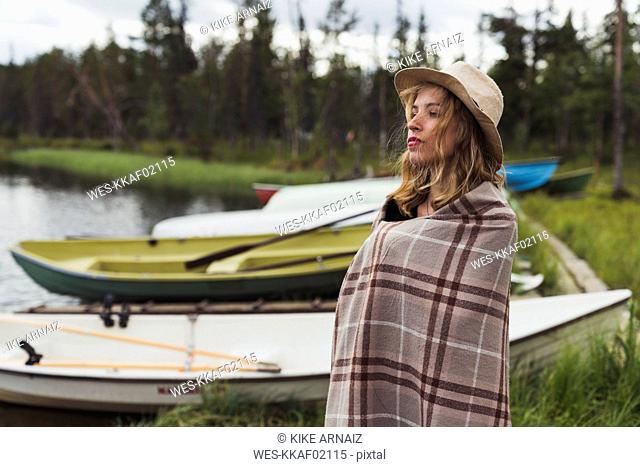 Finland, Lapland, woman wearing a hat wrapped in a blanket standing at the lakeside