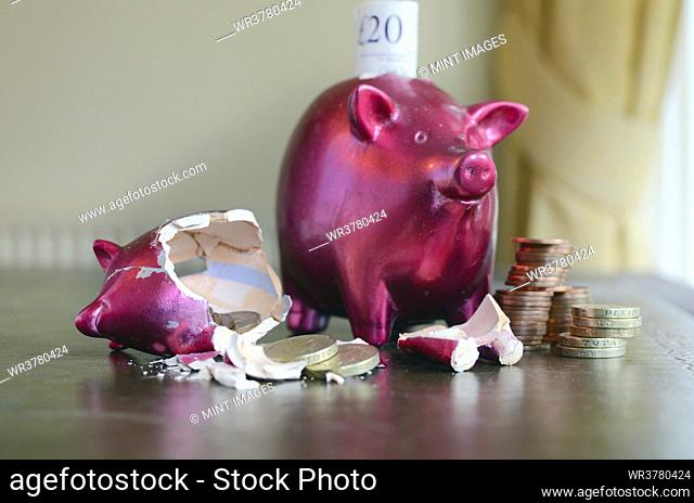 Smashed and whole piggy bank with piles of pounds on table and notes, concept of saving and spending money