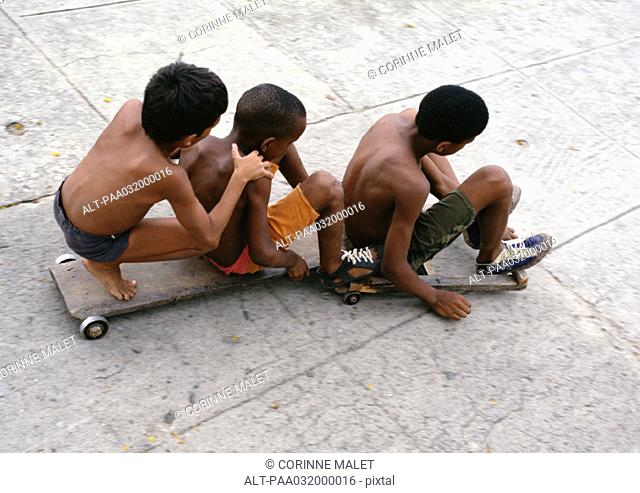 Three boys sitting on skateboards, elevated view