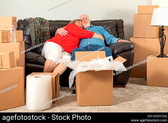 Affectionate Tired Senior Adult Couple Resting on Couch Surrounded By Moving Boxes