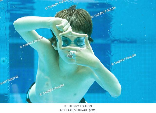 Boy swimming underwater in swimming pool, hands forming finger frame