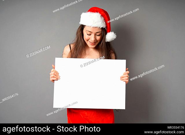female santa looking down at blank sign with copy space - young woman wearing christmas costume