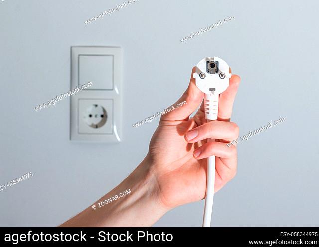 White plug with cable in males hand, ready to connect. Energy concept