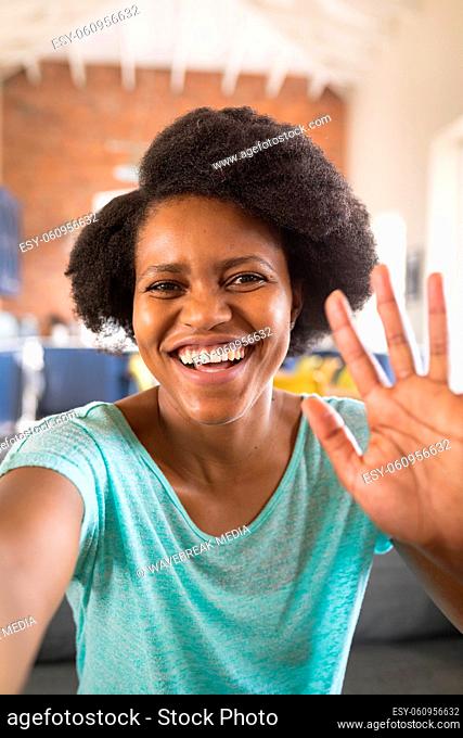 Portrait of happy african american woman waving hand on video call at home