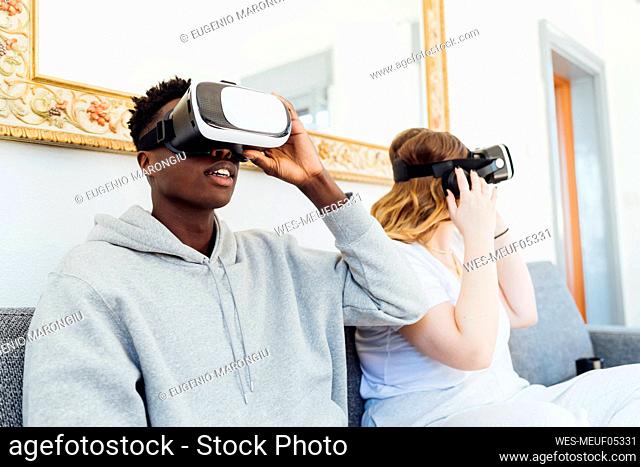 Young couple wearing virtual reality simulators sitting on sofa at home