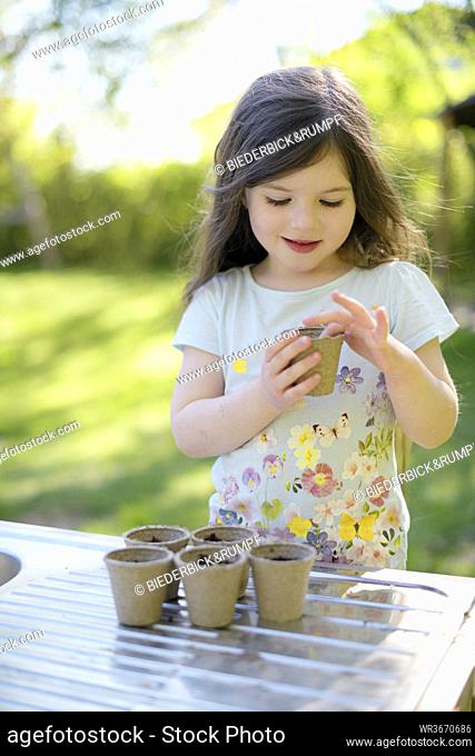 Cute girl planting seeds in small pots on table at garden