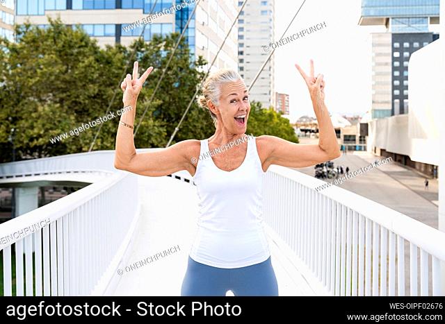 Happy woman showing peace sign standing on footbridge