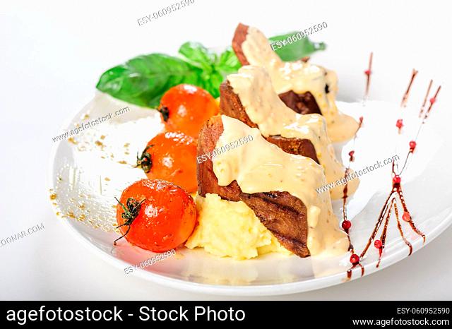 Baked mutton meat with creamy sauce, mashed potato and grilled cherry tomatoes, close up