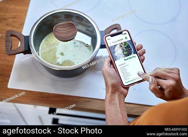 Young woman preparing food through mobile application in kitchen at home
