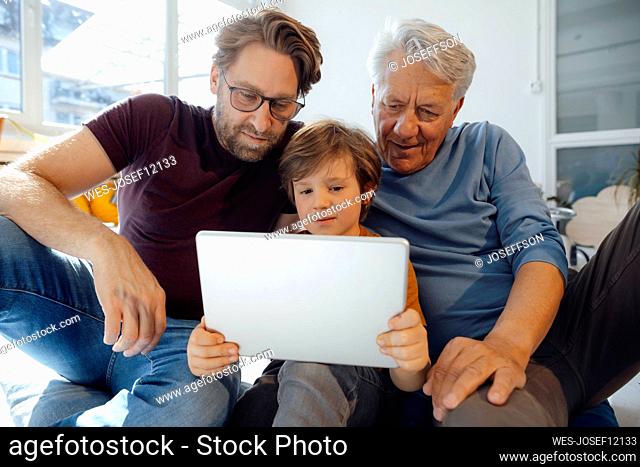 Boy watching movie with father and grandfather on tablet PC at home