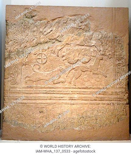 Funerary stele made of porous stone, with relief chariot scene. The spirals in the upper panel may represent waves, thus indicating the coastal location of the...
