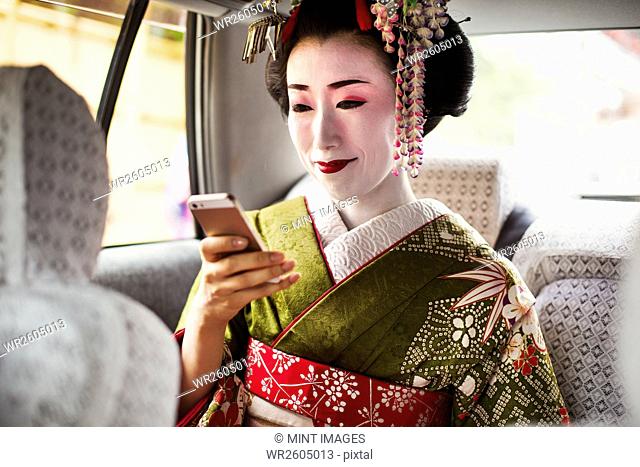 A woman dressed in the traditional geisha style, wearing a kimono and obi, with an elaborate hairstyle and floral hair clips