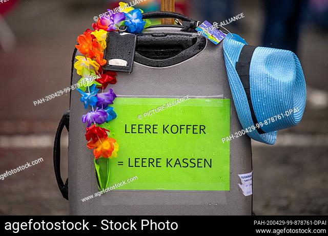 29 April 2020, Bavaria, Munich: Empty suitcases, empty coffers"" is written on a suitcase decorated with a garland and a Fedora hat