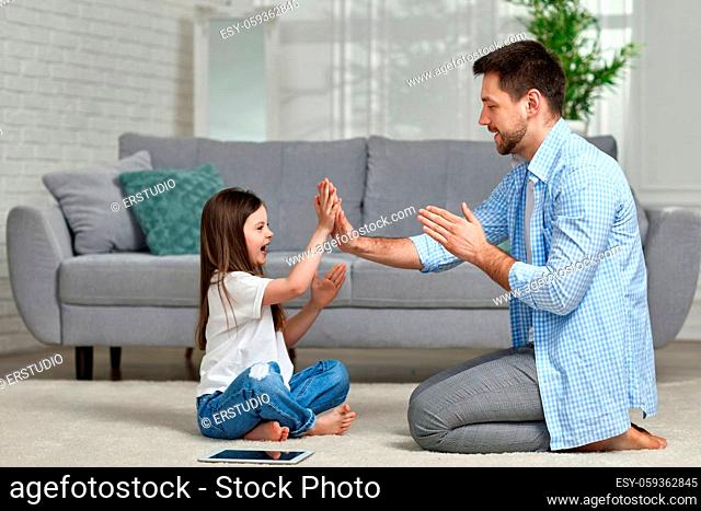 Little kid girl plays with dad at home sitting on white carpet. Father's day