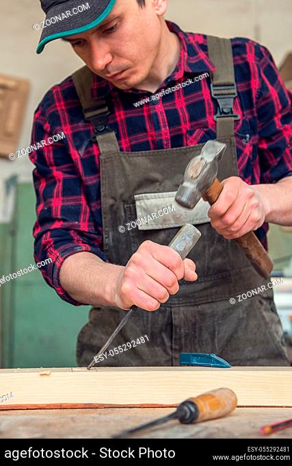 Carpenter working with a chisel and hammer in a wooden workshop. Profession, carpentry and manual woodwork concept
