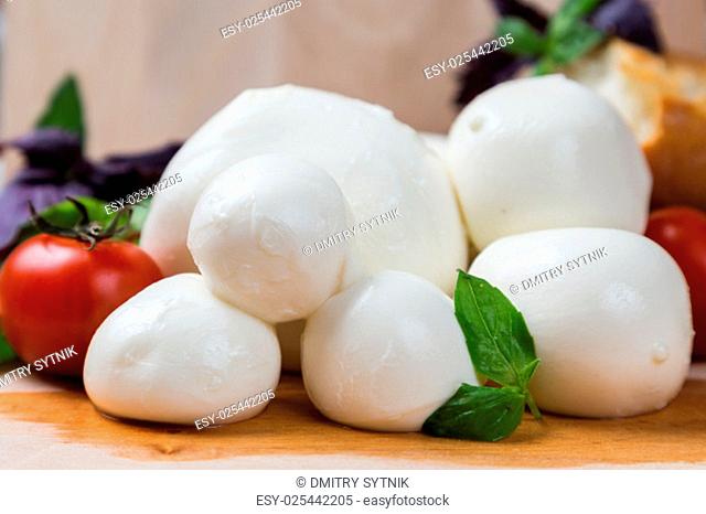 balls mozzarella different size with tomatoes cherry, bread and basil on wooden background