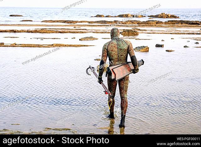 Mature man with harpoon and flipper walking at beach