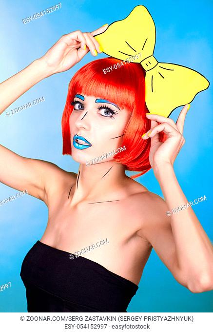 Portrait of young woman in comic pop art make-up style. Female in red wig on blue background. Girl with yellow bow-tie in hands