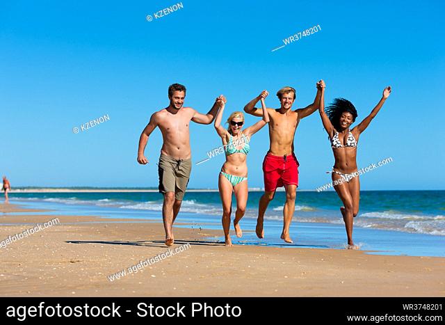 Four friends - men and women - on the beach having lots of fun in their vacation running through the water